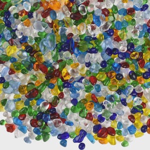 May include: A close-up of a collection of colourful glass pebbles. The pebbles are in various shapes and sizes, with a mix of transparent and opaque colours, including red, blue, green, yellow, and orange. These decorative stones are ideal for crafts and home decor.