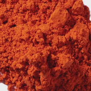 Puede incluir: Primer plano de un mont&oacute;n de polvo naranja brillante. El polvo tiene una textura fina y granulada con grumos visibles y variaciones de tono. El color es un naranja rico y saturado, lo que sugiere un pigmento o tinte.