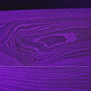 Peut inclure: Gros plan sur une surface en bois violet avec des motifs de grain de bois visibles. Le bois a une couleur violette riche et profonde, avec des nuances plus claires soulignant la texture du grain. La surface est divis&eacute;e par une ligne horizontale.