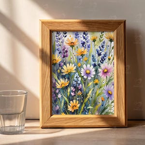 May include: A framed watercolor print featuring a vibrant field of wildflowers in shades of yellow, purple, and pink. The artwork is set in a natural wood frame, creating a rustic aesthetic. The painting captures the beauty of a summer meadow.