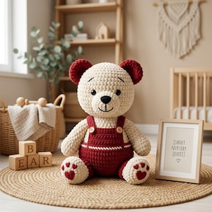 Puede incluir: Un oso de peluche tejido a ganchillo de color crema con orejas de color rojo oscuro y un peto rojo a juego con dos botones de madera. El oso tiene ojos oscuros, una nariz negra bordada y almohadillas en forma de corazón rojo en los pies.