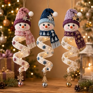 May include: Three hanging snowman ornaments with crocheted hats and scarves in pink, blue, and purple. Each snowman has a long, spiraling white body decorated with small snowflakes and beads, illuminated by internal lights, and finished with a metal bell.