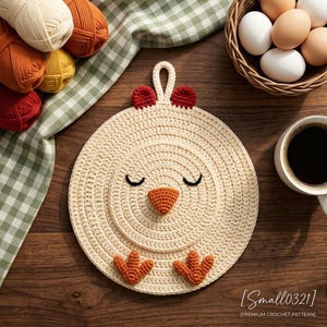 May include: A round, cream-coloured crochet potholder shaped like a chicken face with a small hanging loop. It features a textured orange beak, two small red combs on top, two orange feet at the bottom, and two embroidered black closed eyes.