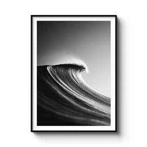 Könnte beinhalten: Schwarz-Weiß-Fotografie einer sich brechenden Meereswelle. Die Welle wird in der Mitte der Krümmung erfasst, mit einer Schaumkrone vor einem Himmel mit Farbverlauf. Das Bild ist in einem schwarzen Rahmen eingefasst.