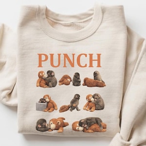 May include: Beige sweatshirt with the word "PUNCH" in orange block letters. The sweatshirt features a repeating pattern of cartoon monkeys in various poses. The monkeys are in shades of brown, gray, and tan.