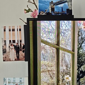 Peut inclure: Un écran Bravia noir affichant une vue de fenêtre sur des arbres, avec trois photographies fixées au cadre. Une photo montre un couple de mariés, une autre un couple, et celle du haut représente le Tower Bridge de Londres au crépuscule.