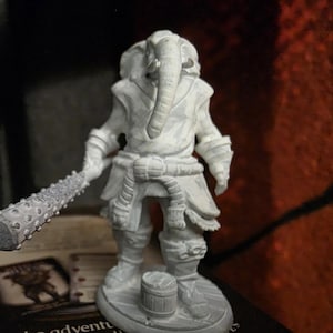 May include: A gray miniature figurine of an elephant-headed warrior holding a spiked club. The figure is wearing armor and a rope belt. A small barrel is at the figure's feet. The figurine is on a round base.