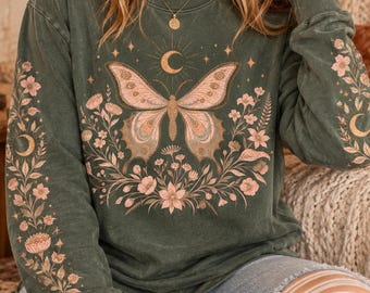 May include: A dark green long-sleeve crewneck sweatshirt featuring a central graphic of a butterfly, a crescent moon, and floral elements. The sleeves are decorated with matching floral vines and small moon motifs in shades of pink and gold.