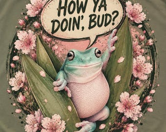 May include: An olive green t-shirt featuring a graphic of a light blue and pink frog perched among green leaves and pink cherry blossoms. A speech bubble above the frog contains the black text, "HOW YA DOIN', BUD?" in a stylized font.