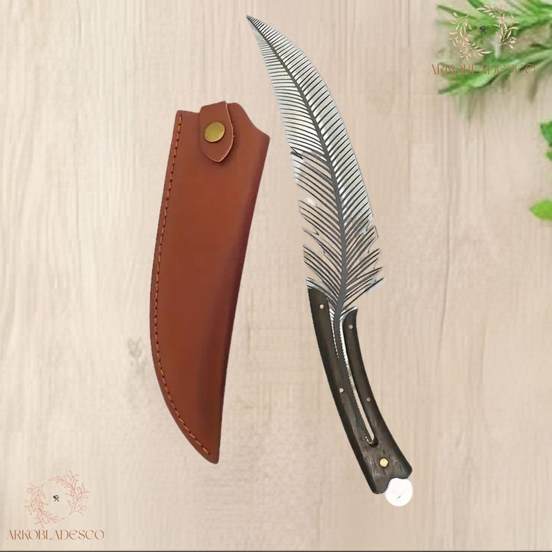 May include: A decorative knife with a feather-shaped blade and a dark wooden handle. The blade is silver and detailed. A brown leather sheath with a snap closure is included. The knife is designed for display or collection.