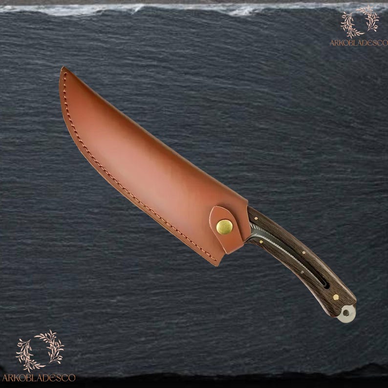 May include: A hunting knife with a brown leather sheath. The knife features a dark wooden handle with metal detailing. The sheath is fastened with a brass-coloured stud. The knife is designed for outdoor use.