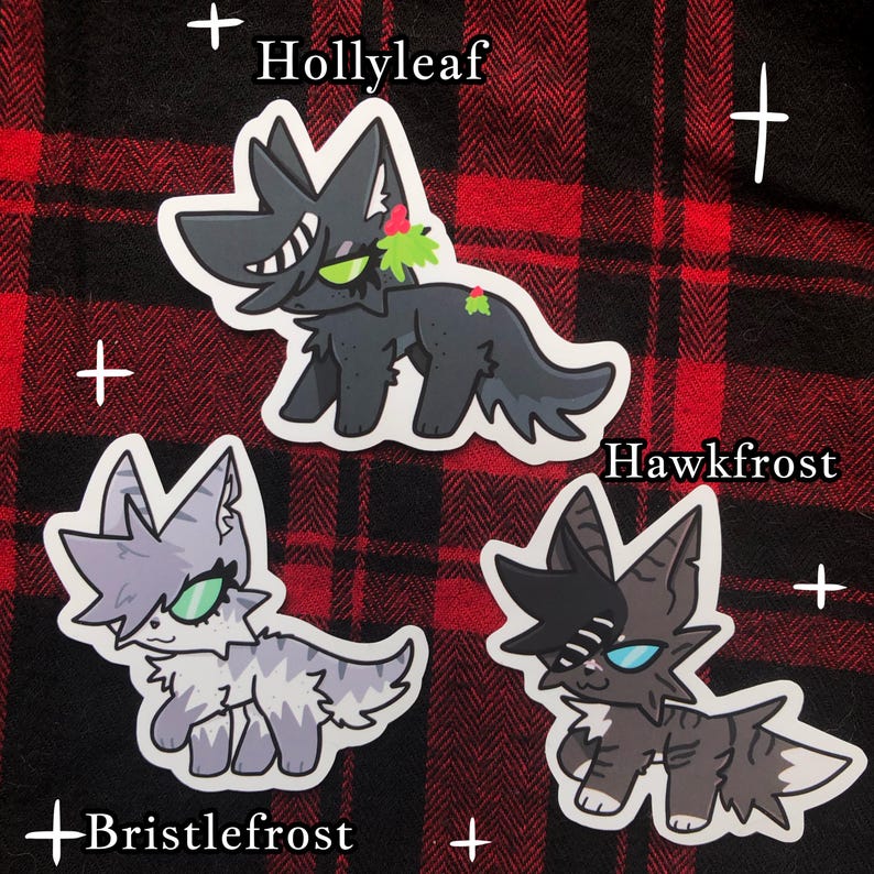 Pu&ograve; includere: Tre adesivi di gatti dei cartoni animati su uno sfondo a scacchi rosso e nero. Gli adesivi presentano diversi disegni di gatti con nomi: Hollyleaf, Hawkfrost e Bristlefrost. Ogni gatto ha colori e segni unici, con il gatto Hollyleaf che indossa un rametto di agrifoglio.