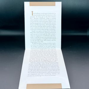 May include: A white rectangular informational card featuring a tan horizontal bar at the top and bottom. The card contains printed text detailing the history and traditional process of glass cutting, starting with the words This brilliant crystal egg.