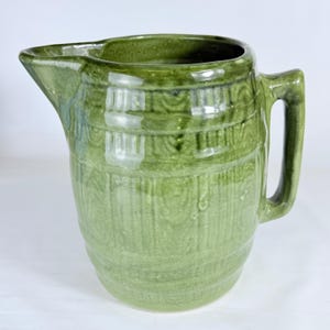 Op de afbeelding: Een groene keramische kan met een tuit en handvat. De kan heeft een textuur met verticale en horizontale patronen. De kan is ongeveer 23 cm hoog.