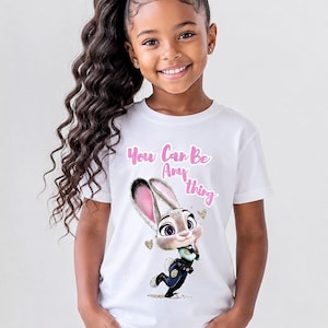 May include: White t-shirt featuring a cartoon image of Judy Hopps from Zootopia, with the text "You Can Be Anything" in pink. The shirt is worn by a young girl with long, curly dark hair and blue jeans.