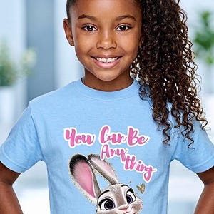 May include: A light blue t-shirt featuring a cartoon image of Judy Hopps from Zootopia, with the text "You Can Be Anything" in pink. The shirt has a crew neck and short sleeves.