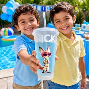 May include: A clear plastic cold cup with a lid and straw, featuring the name NICK in white capital letters and a graphic of a cartoon fox wearing sunglasses and a tropical shirt. The cup is held forward, displaying the character design clearly.