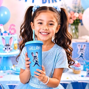May include: A light blue plastic tumbler with a lid and straw, featuring a graphic of a cartoon rabbit and the name KAELANY printed in white. The cup has a smooth finish and is held upright, displaying the character design clearly on the front.