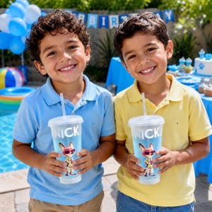 May include: Two clear plastic tumblers with lids and straws, each featuring the text NICK and a graphic of a cartoon fox wearing sunglasses and a floral shirt. The cups are transparent with a light blue tint and hold a cold beverage inside.
