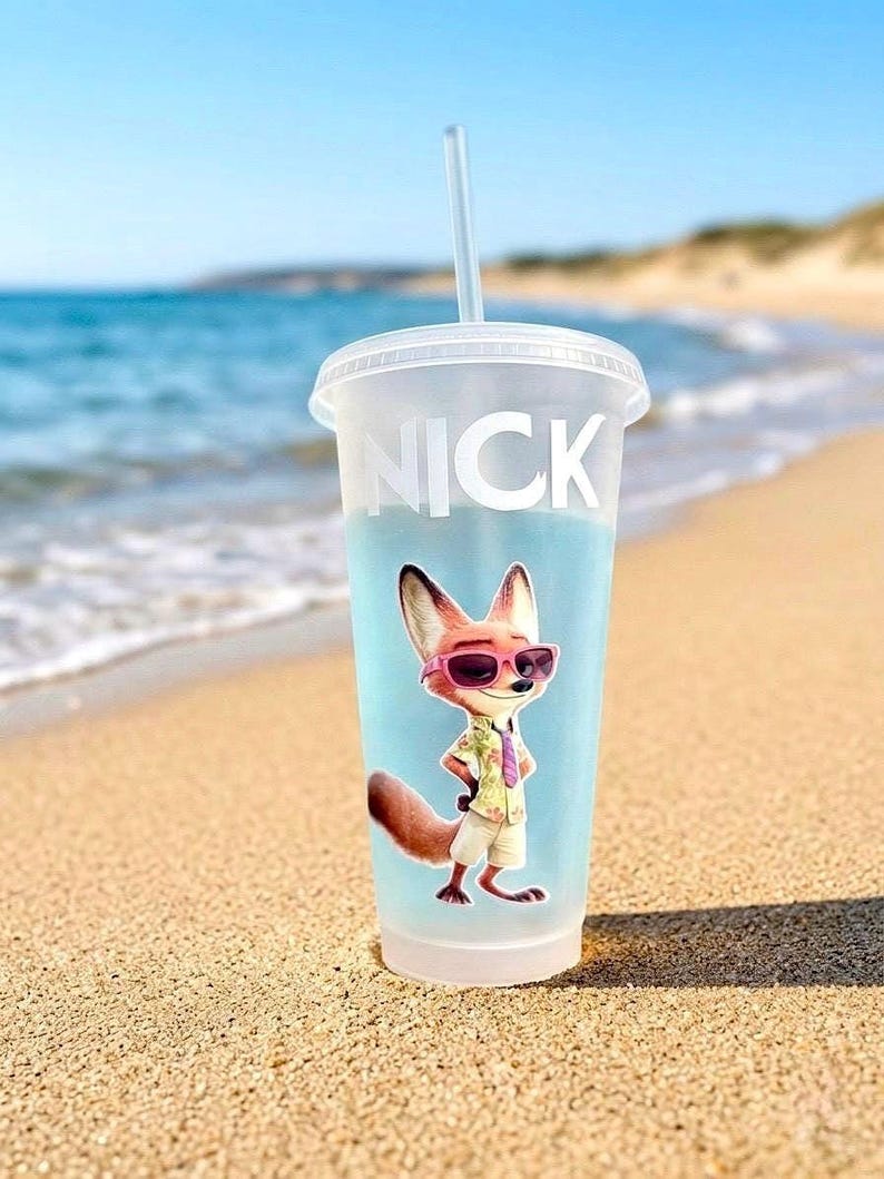 May include: A frosted plastic cold cup with a lid and straw, featuring the name NICK in white capital letters and a graphic of a cartoon fox wearing pink sunglasses, a light-colored patterned shirt, a purple tie, and beige shorts.