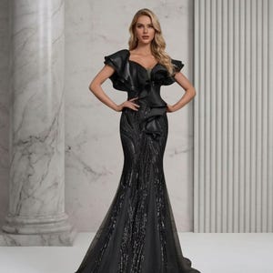 May include: A black evening gown with a mermaid silhouette. The bodice features a ruffled, off-the-shoulder design. The skirt is embellished with sequins and flares out at the bottom. The dress is floor-length and made of a shimmering fabric.