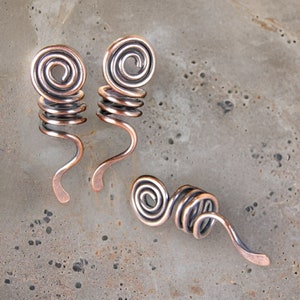 May include: Three copper wire hair coils, each with a spiral design. The coils are in various shapes and sizes.