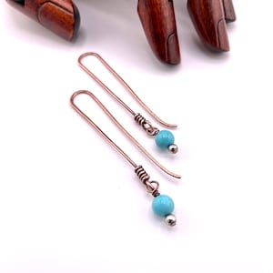 May include: A pair of copper earrings with turquoise beads. The earrings are long and dangle.