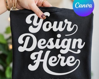 May include: A black t-shirt featuring the white text Your Design Here in a bold, cursive font. The shirt is held up, displaying the front graphic clearly. The design is centred on the fabric, providing a blank space for custom artwork or logos.