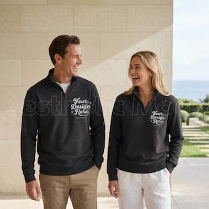 May include: Two people wearing charcoal gray quarter-zip pullovers. The pullovers have the text "Your Design Here" printed on the front. The background features a stone wall and a view of the ocean.