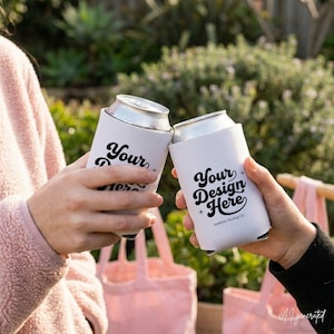 May include: Two white foam can coolers, each holding a silver aluminum beverage can. The coolers feature black cursive text that reads Your Design Here, accompanied by small star icons. The text is printed in a bold, retro-inspired font style.