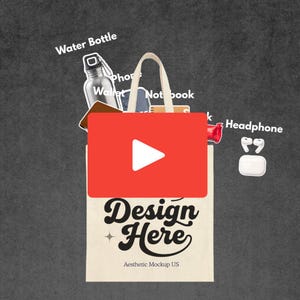 May include: A beige tote bag with the text "Design Here" and a play button overlay. The bag contains a water bottle, wallet, notebook, phone, headphones, and a small red item. The bag is on a gray background.