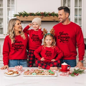 May include: A family of four wearing matching red sweatshirts with the text "Your Design Here". The children are wearing plaid pajamas. A table is set with cookies, candy canes, and a red mug.