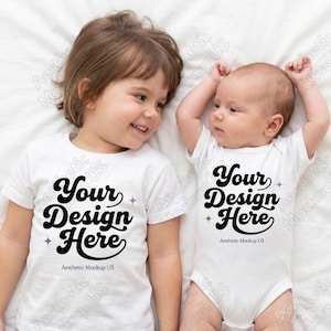 May include: A white short-sleeved t-shirt and a white short-sleeved baby bodysuit, both featuring the black text "Your Design Here" in a stylized script font, accompanied by small four-pointed star icons and the text "Aesthetic Mockup US".
