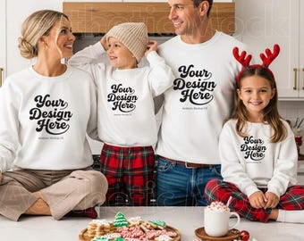 May include: A family of four wearing matching white sweatshirts with the text "Your Design Here". The child on the right wears a red headband with reindeer antlers. A wooden tray holds decorated Christmas cookies.