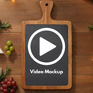 May include: A wooden cutting board with a black slate center and a handle. A white play button is centered on the slate, with the words "Video Mockup" below it. The board is on a wooden surface, with grapes and rosemary sprigs.