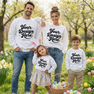 Op de afbeelding: Een gezin van vier personen draagt bijpassende witte sweatshirts met lange mouwen en de zwarte tekst Your Design Here op de voorkant. De groep bestaat uit twee volwassenen, een kind met een bloemenrok en konijnenoren en een kind in een kaki broek.