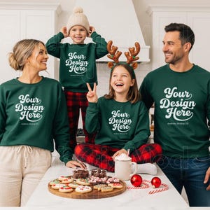 Könnte beinhalten: Eine Familie in passenden dunkelgrünen Sweatshirts mit dem weißen Text "Your Design Here". Sie versammeln sich um einen Tisch mit Weihnachtsplätzchen und Dekorationen. Die Kinder tragen Rentiergeweihe und eine Mütze.