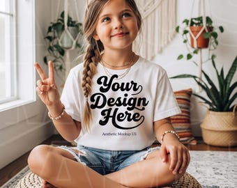 May include: A white short-sleeved t-shirt featuring the black text Your Design Here and Aesthetic Mockup US, worn with blue denim shorts. The shirt is styled with heart-shaped sunglasses, a beaded bracelet, and a braided hairstyle.