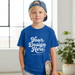 K&ouml;nnte beinhalten: Ein blaues T-Shirt mit dem Text "Your Design Here" in wei&szlig;er Schrift. Das T-Shirt wird von einer Person getragen, die eine blaue Jeans-Baseballkappe tr&auml;gt. Der Text "Aesthetic Mockup US" steht darunter.