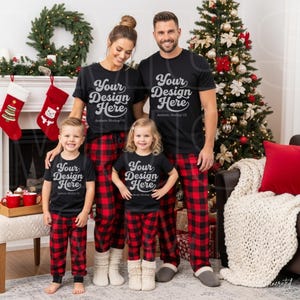 Pode incluir: Uma família de quatro pessoas veste camisetas pretas combinando com o texto branco Your Design Here e calças de pijama xadrez vermelhas e pretas. As camisetas têm mangas curtas e gola redonda, enquanto as calças têm um corte relaxado.