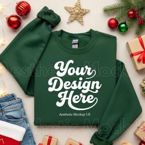 May include: A dark green sweatshirt with the text "Your Design Here" in white script. The sweatshirt is surrounded by Christmas decorations, including ornaments, a star, and wrapped gifts. The text "Aesthetic Mockup US" is also visible.