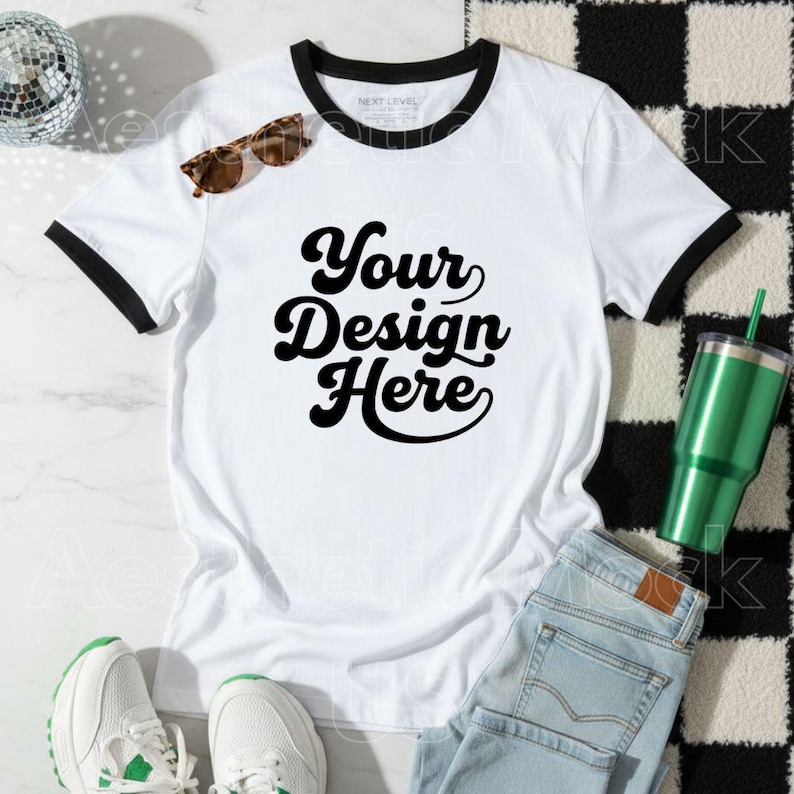 May include: A white ringer t-shirt with black trim and the text "Your Design Here" in a bold, retro font. The shirt is paired with light blue jeans, white trainers, and sunglasses. A green tumbler and a disco ball are also in the image.