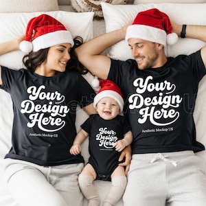 Könnte beinhalten: Zwei schwarze T-Shirts und ein schwarzer Baby-Body, jeweils mit dem weißen Text 'Your Design Here' und 'Aesthetic Mockup US' bedruckt. Die Kleidung wird mit rot-weißen Weihnachtsmannmützen, hellgrauen Hosen und weißen Socken kombiniert.