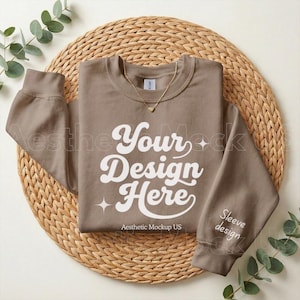 May include: A brown sweatshirt with the text "Your Design Here" in white script. The sleeve has the words "Sleeve design" printed on it. A gold necklace with a heart pendant is on the sweatshirt. The sweatshirt is on a woven mat.