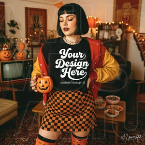 Puede incluir: Una camiseta negra con el texto blanco "Your Design Here" y "Aesthetic Mockup US" impreso en el frente. La camiseta se lleva con una chaqueta universitaria roja y amarilla y una falda a cuadros naranja y negra, mientras se sostiene una taza de calabaza.