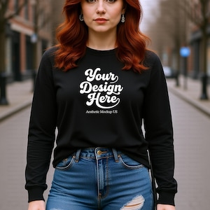 May include: Black long-sleeve shirt with the text "Your Design Here" in white script. The shirt is paired with blue denim jeans. The text "Aesthetic Mockup US" is below the main text.