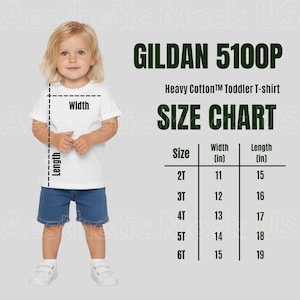 Puede incluir: Un niño con una camiseta blanca y pantalones cortos de mezclilla azules. La imagen incluye una tabla de tallas para camisetas para niños pequeños Gildan 5100P Heavy Cotton, con medidas en pulgadas (27.94cm a 38.1cm de ancho).