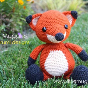 May include: A handmade orange crochet fox amigurumi with black accents on the ears, paws, and nose. The fox has a white belly and black button eyes. The text "Little Muggles amigurumi designs" is visible.