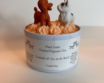 May include: A scented candle in a light blue tin, topped with orange-colored wax and two dog figurines. The candle has text that reads "Dual Scents, Natural Fragrance Oils, Lavender & Sex on the Beach, Candle/8oz."