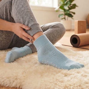 Puede incluir: Un par de calcetines tobilleros de color azul claro con puño acanalado y pequeños patrones de agarre de silicona blanca en forma de flor en las suelas. Los calcetines están hechos de un tejido suave y proporcionan tracción.